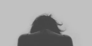Silhouette scura di una persona vista di spalle con la testa china per rappresentare il senso di colpa